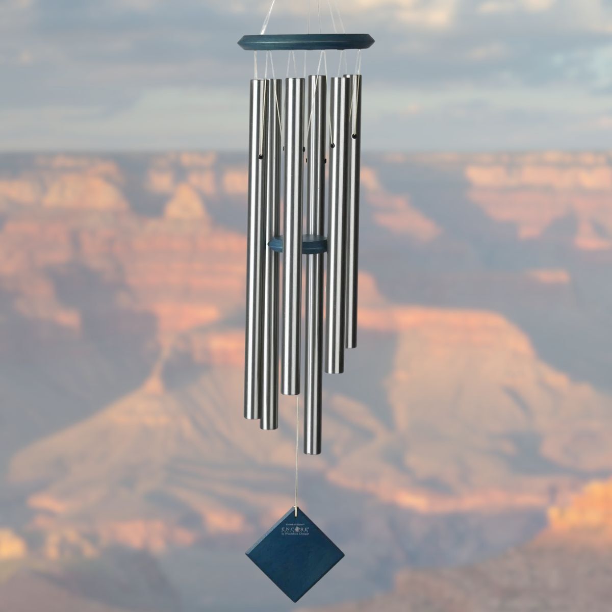 Woodstock brand 'Chimes of the Eclipse' SILVER aluminum tubes wind chime that is 37 inches in length, with customizable BLUE WASH wooden wind sail displayed in front of a landscape background