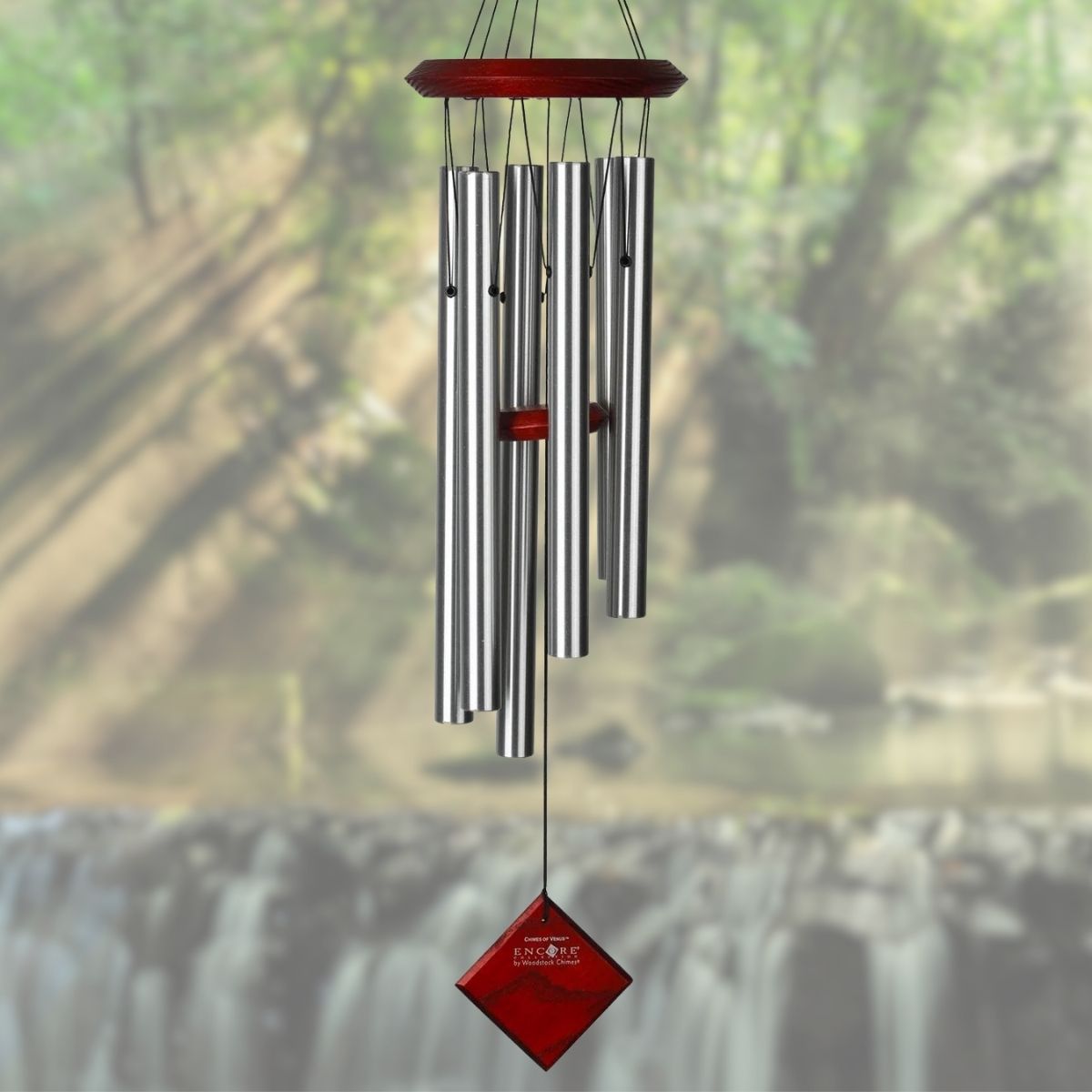 Woodstock brand 'Chimes of the Eclipse' silver aluminum tubes wind chime that is 27 inches in length, with customizable red stained wooden wind sail displayed in front of a landscape background