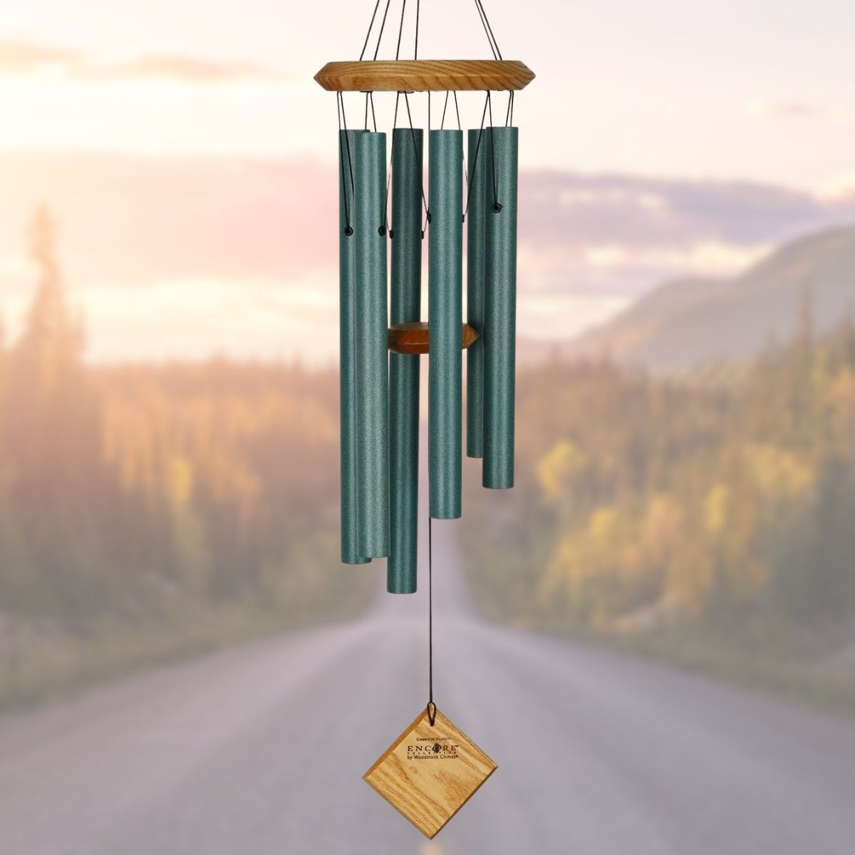 Woodstock brand 'Chimes of the Eclipse' green aluminum tubes wind chime that is 27 inches in length, with customizable lightly stained wooden wind sail displayed in front of a landscape background