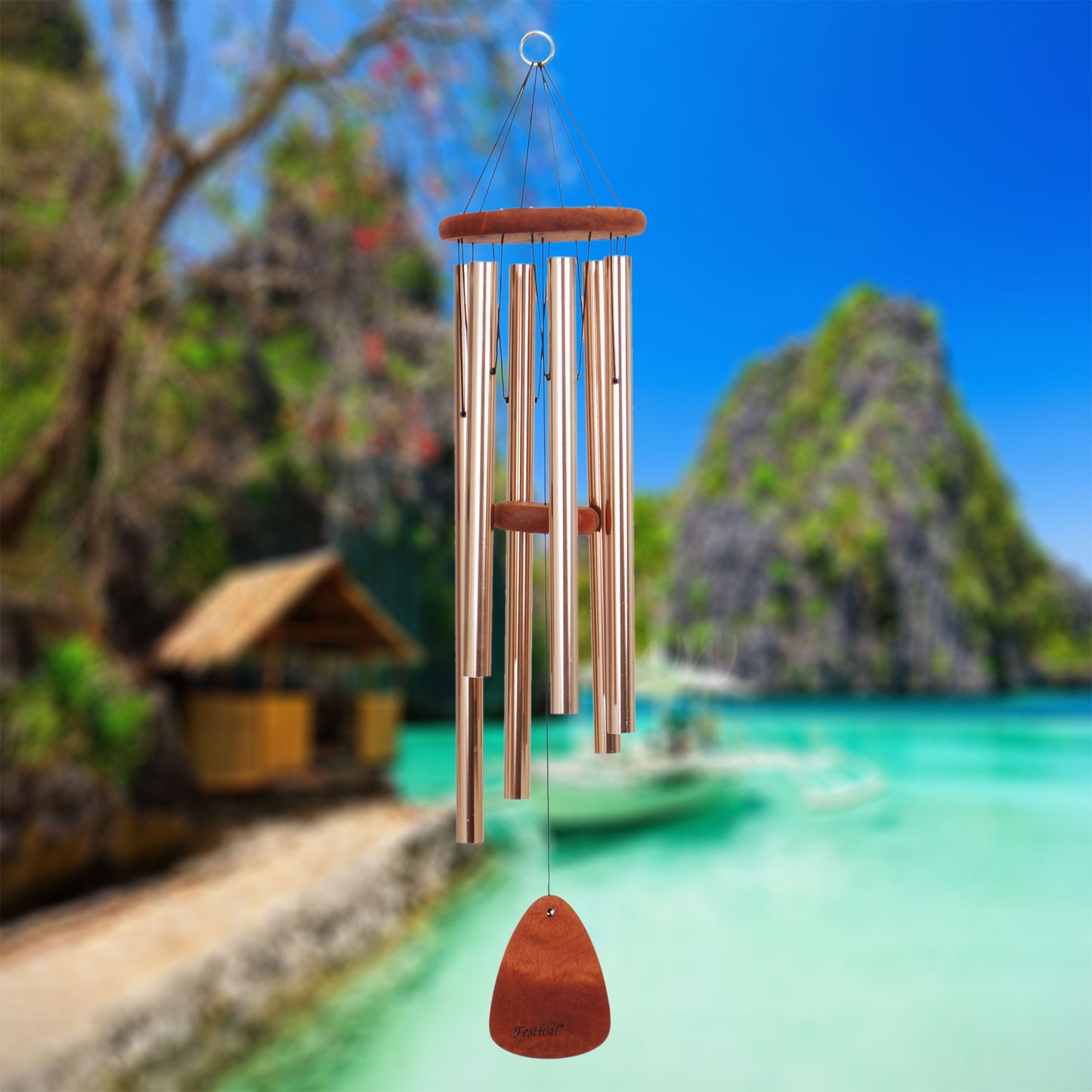 Festival 36 inch bronze wind chime with wooden striker and wind sail, with a scenic background of a tropical island and turquoise water.