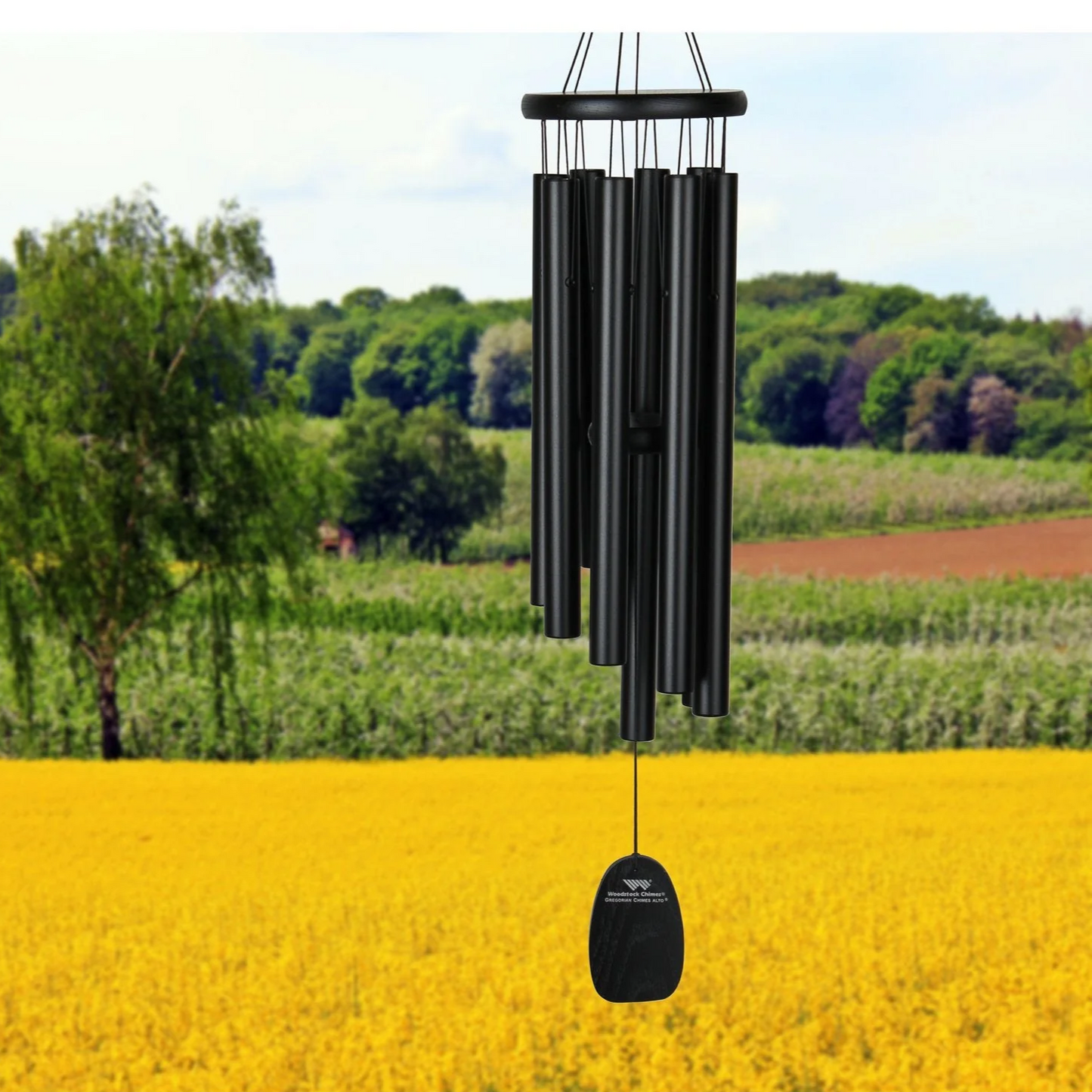 Black Woodstock 27 inch Gregorian Chimes Alto wind chime, black tubes and black accents, with a background of a yellow grass field with trees and blue sky