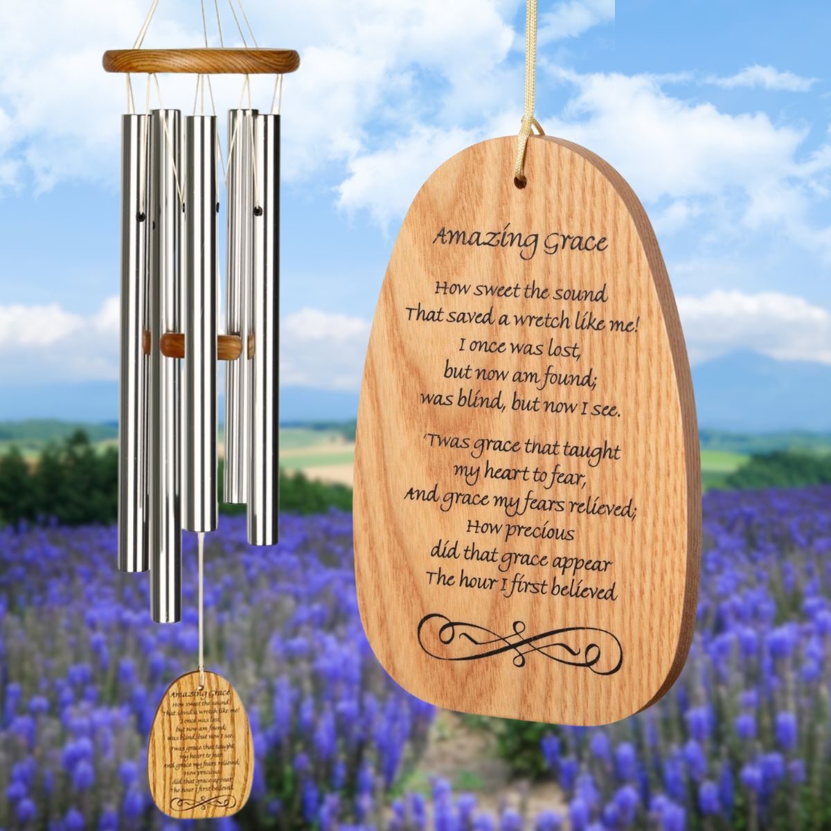 Woodstock Reflections Amazing Grace wind chime with silver tubes and an inscription on the wind sail that reads "Amazing Grace, How sweet the sound
That saved a wretch like me!
I once was lost, but now am found;
was blind, but now I see.
'Twas grace that taught my heart to fear,
And grace my fears relieved;
How precious did that grace appear
The hour I first believed." on a blurred background of a field of blue flowers and blue sky