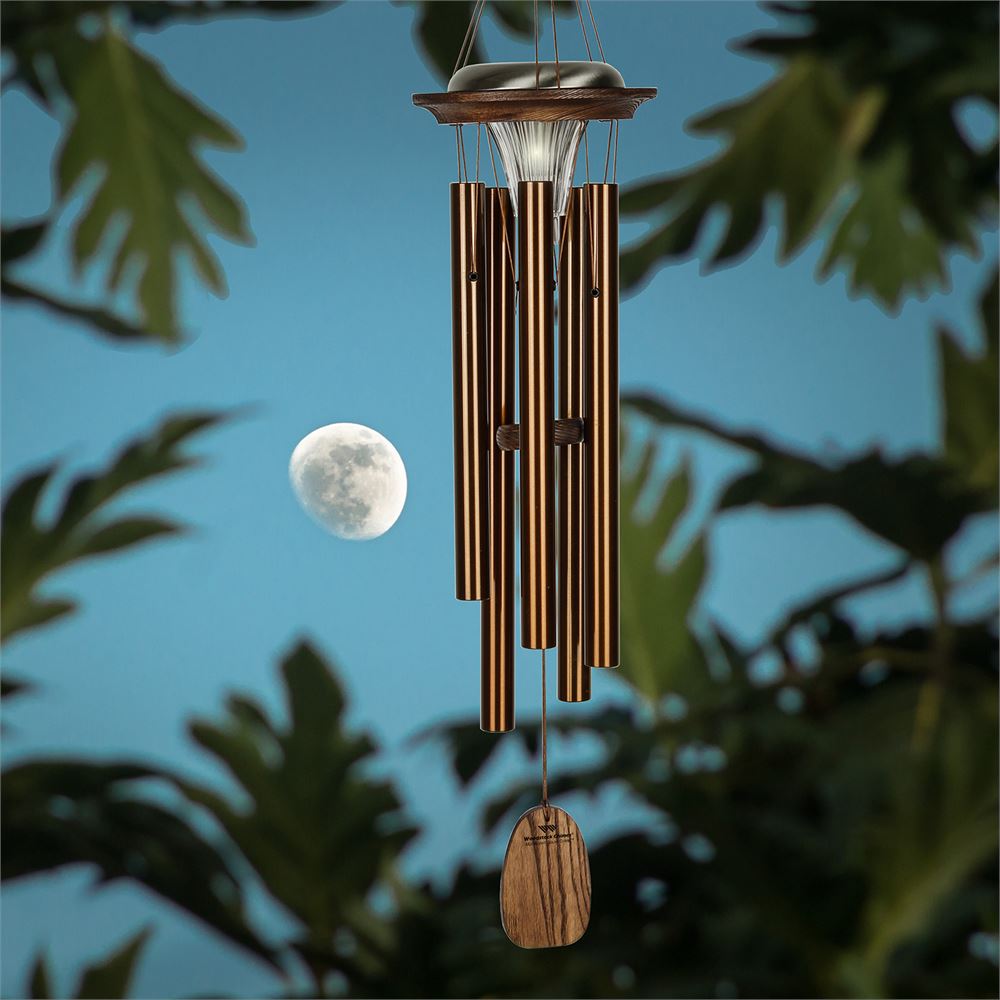 Woodstock Chimes Moonlight Solar Chime in bronze finish, featuring six aluminum tubes, a solar-powered LED light, and a customizable wind sail displayed on a landscape background