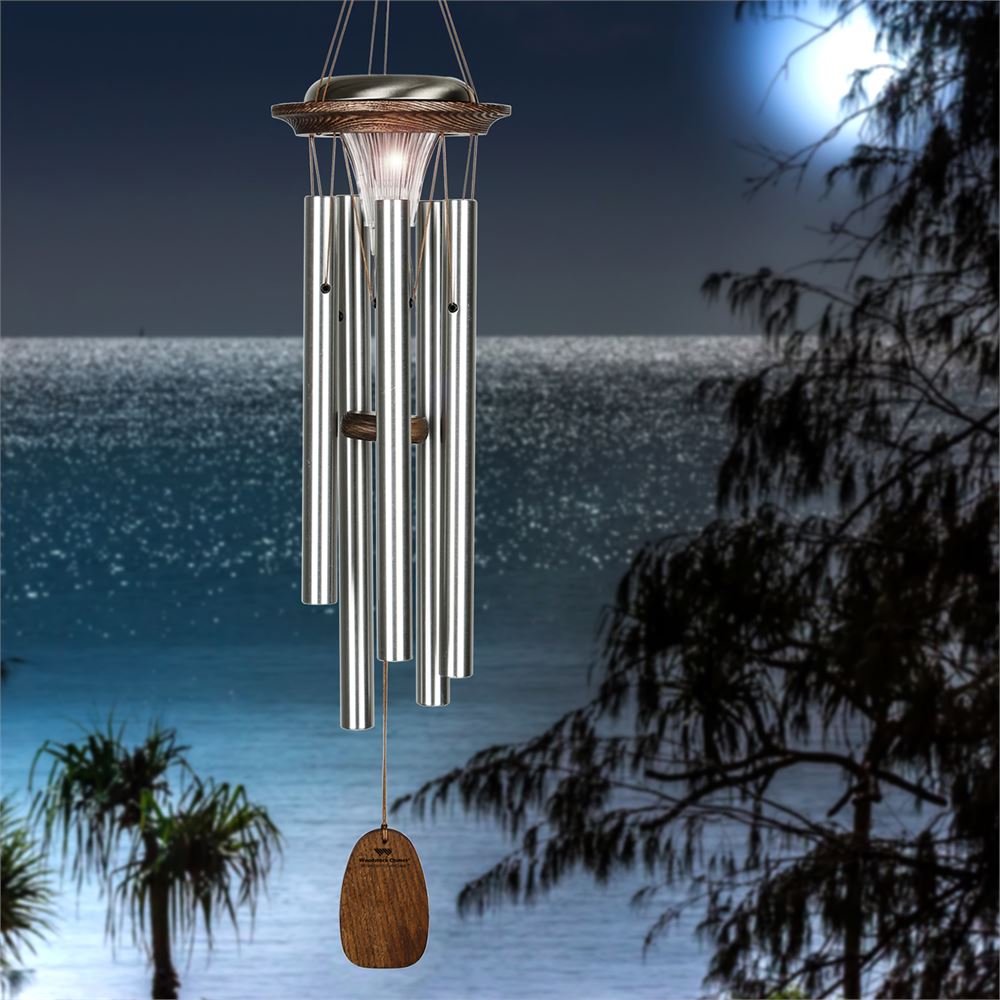 Woodstock Chimes Moonlight Solar Chime in silver finish, featuring six aluminum tubes, a solar-powered LED light, and a customizable wind sail displayed on a landscape background
