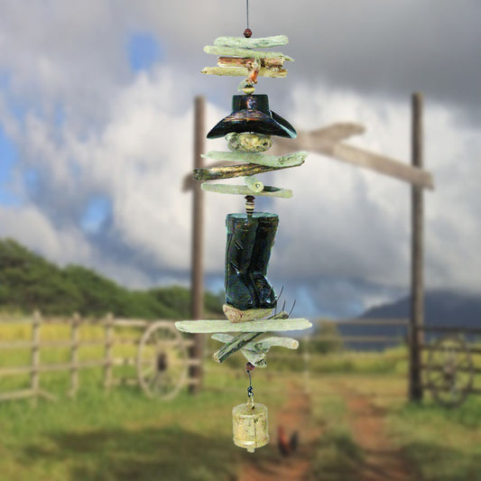 Wooden boot AND COWBOY shaped ornamentS AND DRIFTWOOD PIECES WITH A BELL WIND SAIL with 'Whimsical Winds' branding against a green foliage background.
