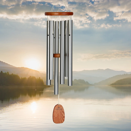 Woodstock brand 'Amazing Grace' wind chime with silver aluminum tubes that is 25 inches in length, with customizable orange wooden wind sail displayed in front of a nature landscape photo