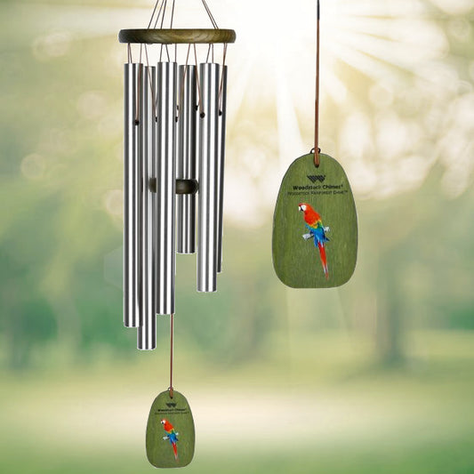 Woodstock Rainforest 24-Inch Wind Chime BEING A 24 INCH hanging chime featuring five SILVER‑tone aluminum tubes suspended from a soft green wash ash‑wood top, with a decorative windcatcher painted with a vivid scarlet macaw motif DISPLAYED IN FRONT OF A LANDSCAPE BACKGROUND