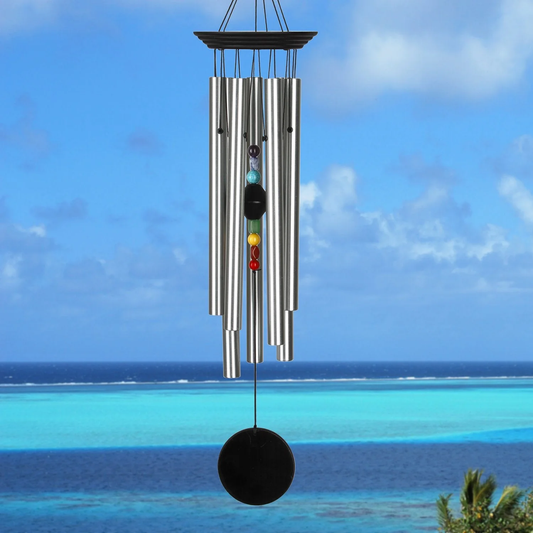 Woodstock Percussion 7‑Stone Bronze Chakra Wind Chime with engravable wooden wind sail WITH seven SILVER aluminum tubes hang from BLACK WASH finish ash‑wood top; the faceted clapper aligns seven chakra stones vertically, with a round wooden sail below that can be personalized with up to 50 characters