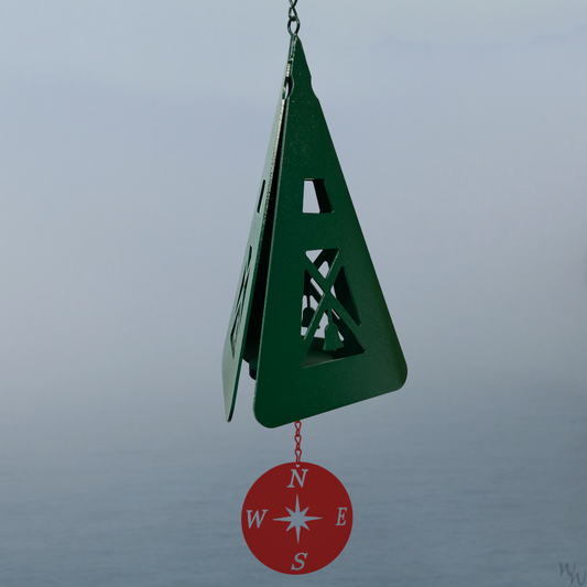 North Country Compass Rose Starboard Green Buoy Bell wind bell featuring a 14‑inch powder‑coated green steel bell, triangular green compass‑rose windcatcher with red compass star, suspended from jack chain; total length approx. 30 inches; single‐tone coastal‑inspired bell made in USA DISPLAYED IN FRONT OF A LANDSCAPE BACKGROUND