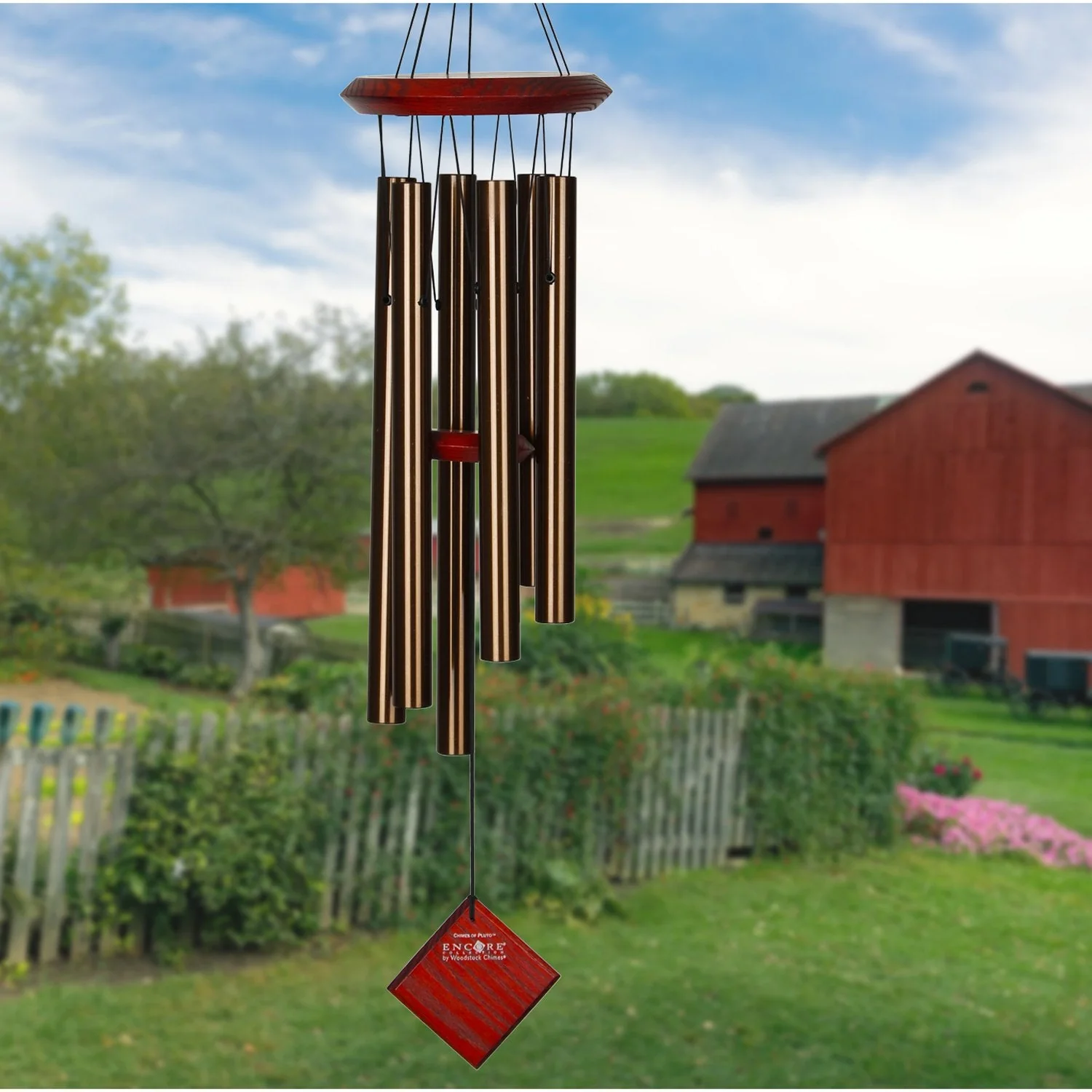 Woodstock brand 'Chimes of the Eclipse' bronze aluminum tubes wind chime that is 27 inches in length, with customizable red wooden wind sail displayed in front of a landscape background 