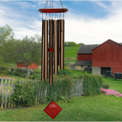 Woodstock brand 'Chimes of the Eclipse' bronze aluminum tubes wind chime that is 27 inches in length, with customizable red wooden wind sail displayed in front of a landscape background 