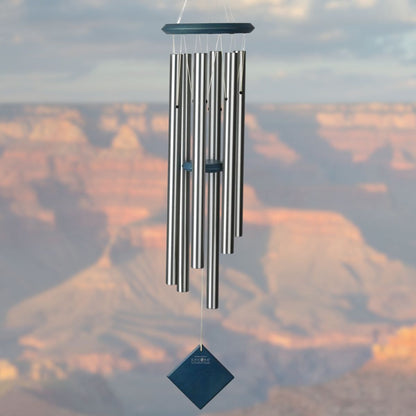Woodstock brand 'Chimes of the Eclipse' SILVER aluminum tubes wind chime that is 37 inches in length, with customizable BLUE WASH wooden wind sail displayed in front of a landscape background 