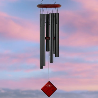 Woodstock brand 'Chimes of the Eclipse' black aluminum tubes wind chime that is 27 inches in length, with customizable red stained wooden wind sail displayed in front of a landscape background