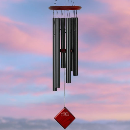 Woodstock brand 'Chimes of the Eclipse' black aluminum tubes wind chime that is 27 inches in length, with customizable red stained wooden wind sail displayed in front of a landscape background
