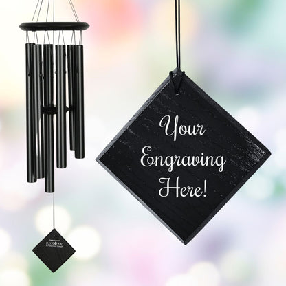 Woodstock brand 'Chimes of the Eclipse' black aluminum tubes wind chime that is 27 inches in length, with customizable black stained wooden wind sail, shown with placeholder text 'Your Engraving Here!' displayed in front of a watercolor background