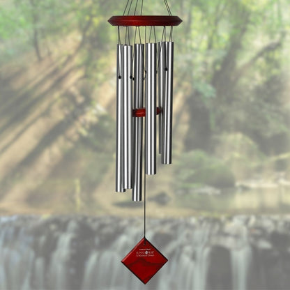 Woodstock brand 'Chimes of the Eclipse' silver aluminum tubes wind chime that is 27 inches in length, with customizable red stained wooden wind sail displayed in front of a landscape background