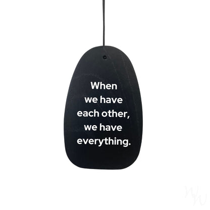 Black wooden wind sail with white text on the wind sail that reads "When we have each other, we have everything." used as an example engraving.