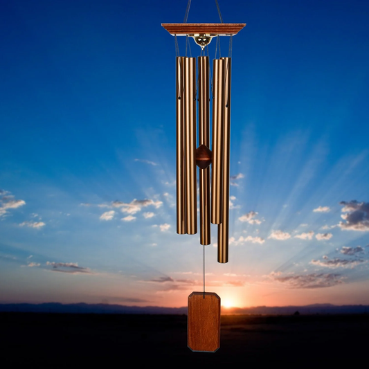 Woodstock Chimes Memorial Chime Large WITH five bronze‑tone aluminum tubes suspended from a teak‑finish ash wood top, with a rectangular wooden windcatcher and a weatherproof compartment beneath the top for storing a keepsake urn DISPLAYED IN FRONT OF A SUNSET LANDSCAPE BACKGROUND